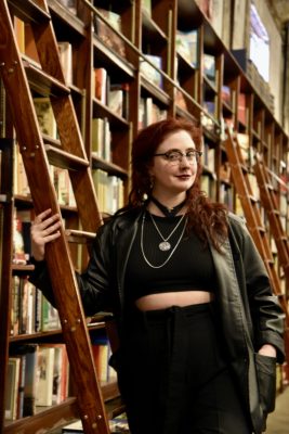 Local bookstore employee in front of a ladder and a shelf of books.