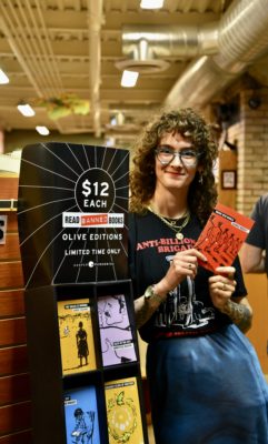 Local bookstore employee stands near shelf of banned books.