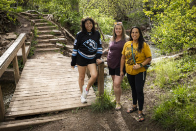 Sapphic Hikers by a bridge in the woods