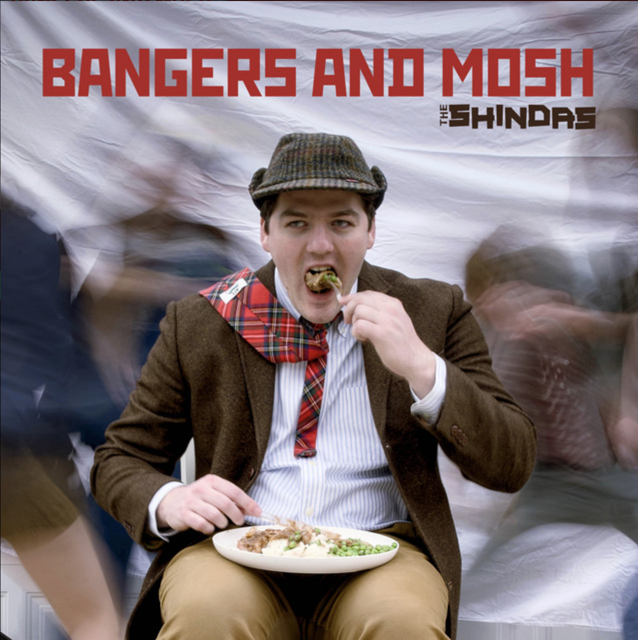 The album Bangers and Mosh by the Shindas -- a British-looking man in a hat and a plaid tie eating bangers and mash, the space behind him a blur of movement.