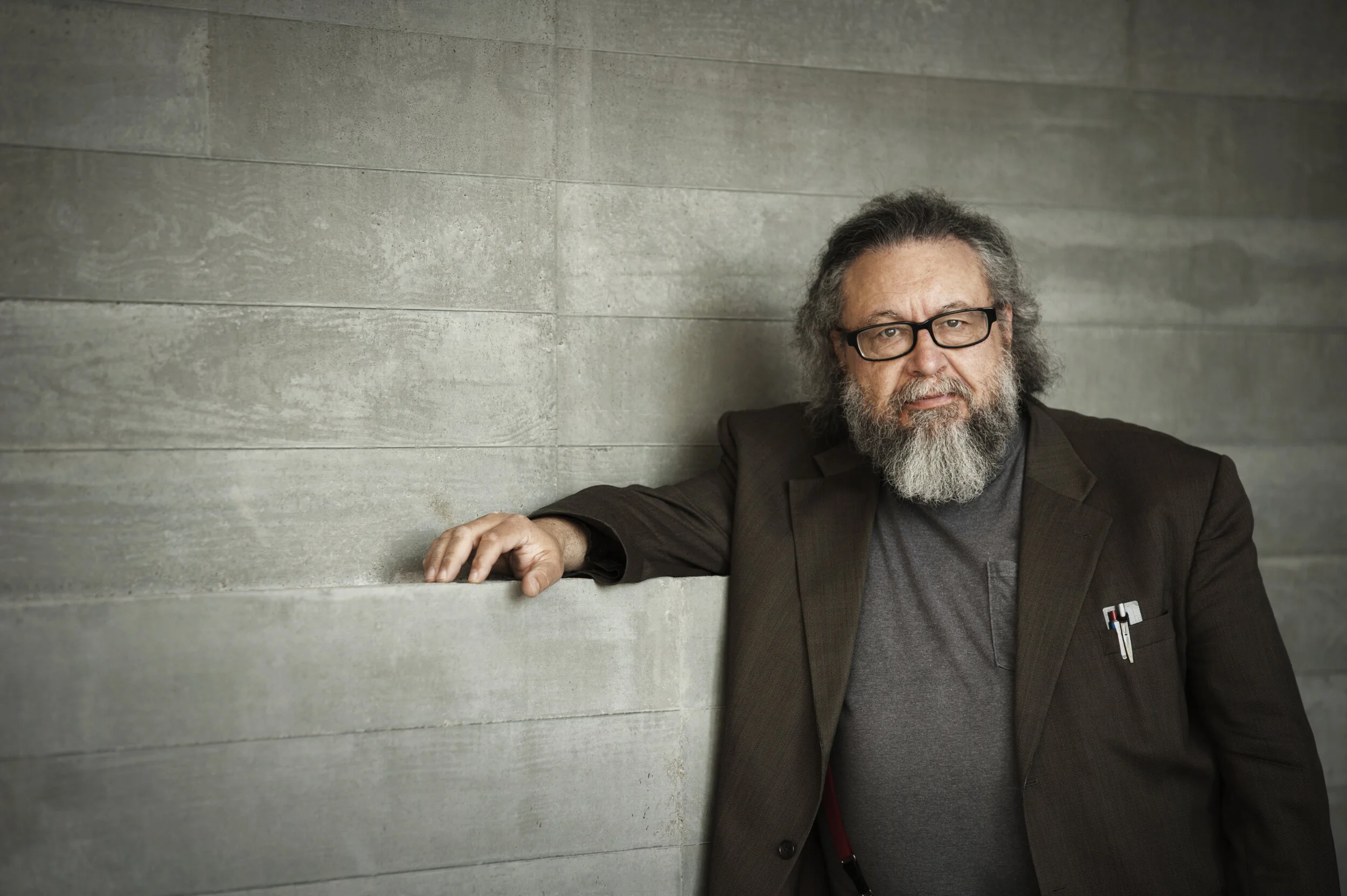 Alex Caldiero with his arm on a ledge against a gray wall