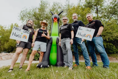 Five men and a blown-up dragon holding signs that say "Free hugs."