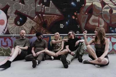 Five bandmates sitting in an alleyway smoking cigarettes.